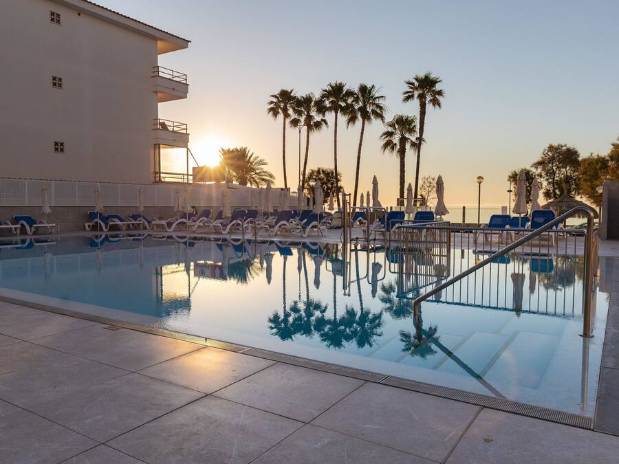 A swimming pool with lounge chairs and palm trees, surrounded by a building with balconies.