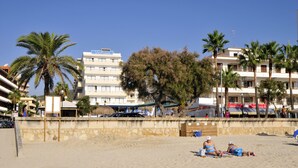 A beach with palm trees, a sandy shore, and a building with balconies. - R2 Verónica (Sant Llorenc des Cardassar)