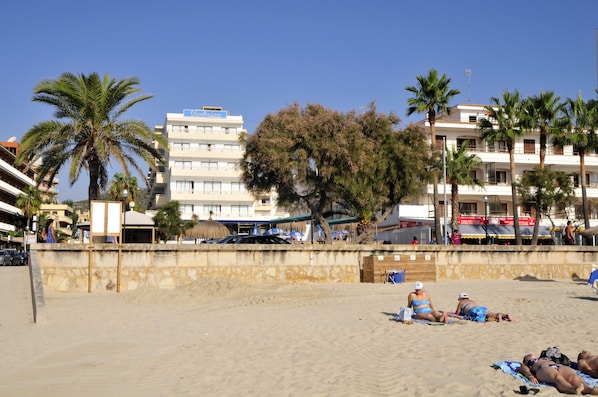 A beach with palm trees, a sandy shore, and a building with balconies. - R2 Verónica (Sant Llorenc des Cardassar)