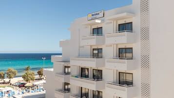 Un hotel de varios pisos con balcones que dan a una playa y al mar.