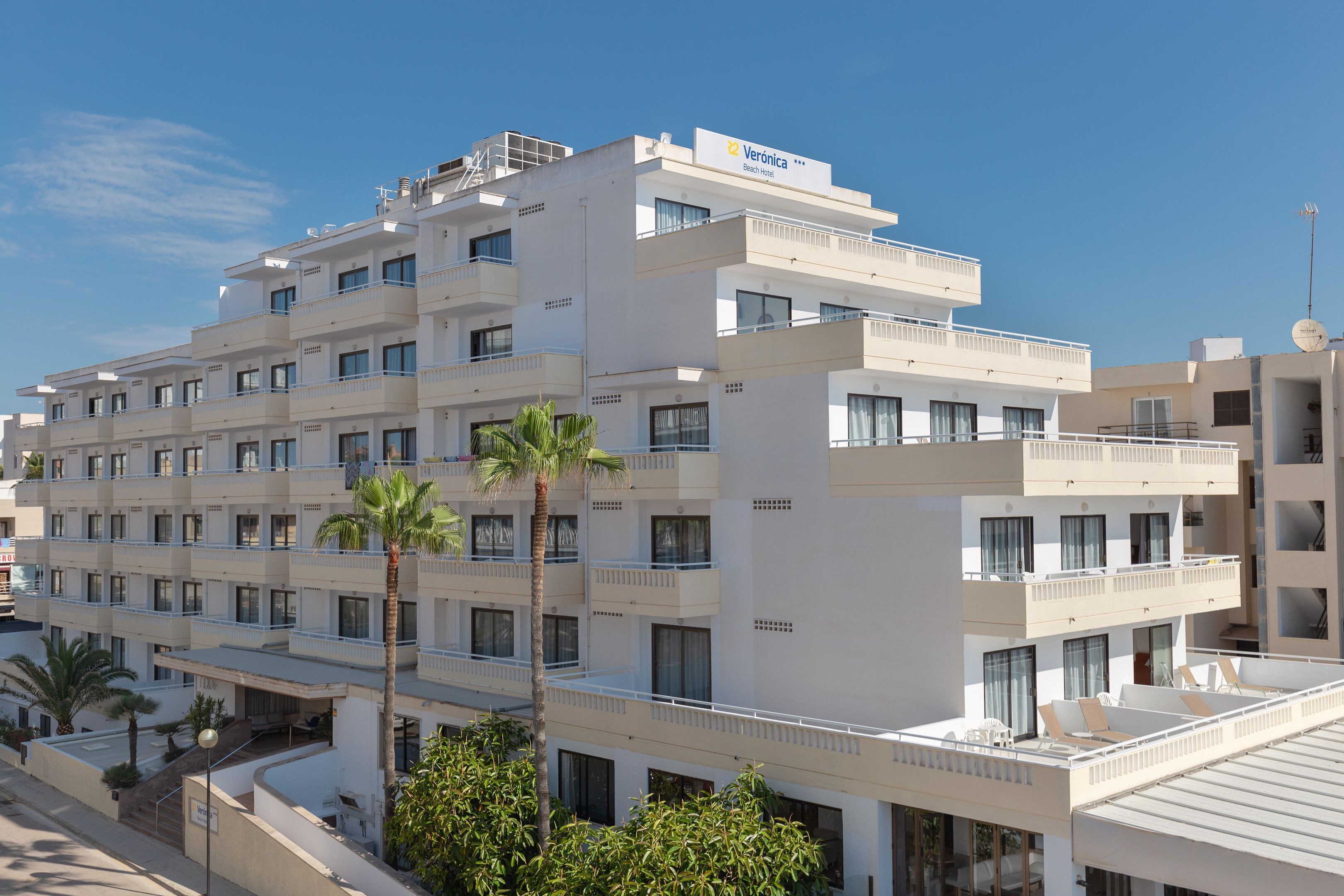 Un hotel de varios pisos con balcones, palmeras y un cielo despejado.