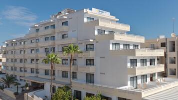 Un hotel de varios pisos con balcones, palmeras y un cielo despejado.