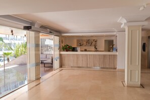 Un moderno vestíbulo de hotel con mostrador de recepción, zona de estar y puertas de cristal que dan al exterior.