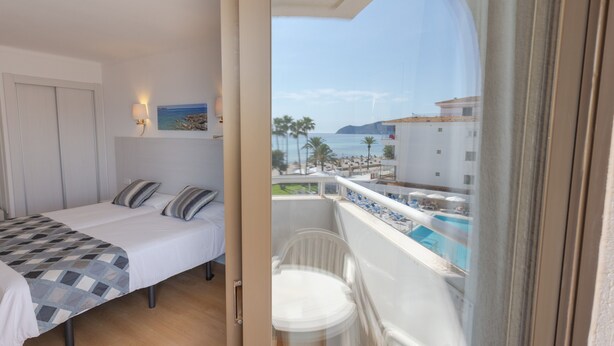 A hotel room with a bed, a small table, and a view of a pool and beach. - R2 Verónica (Sant Llorenc des Cardassar)