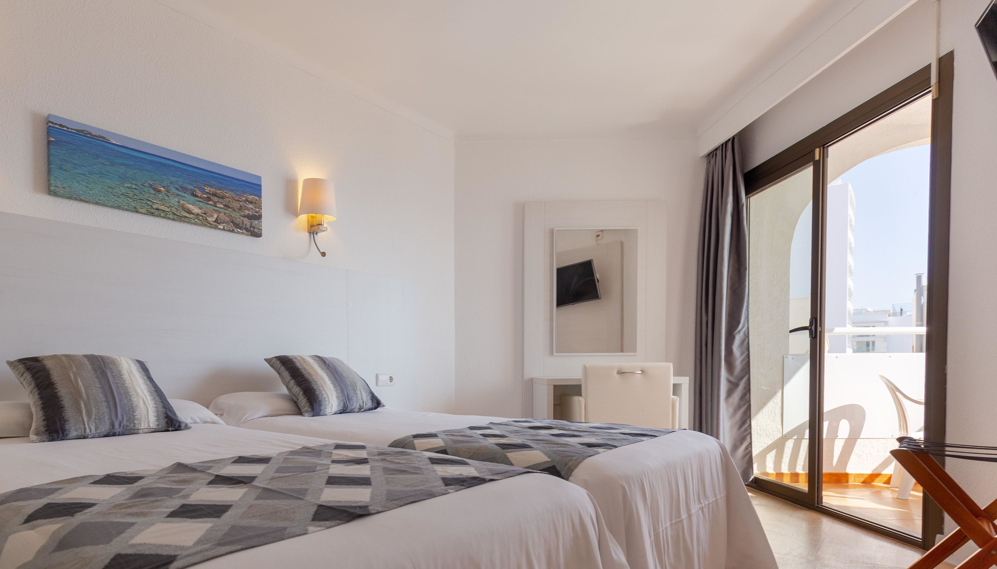 Habitación de hotel con dos camas, un cuadro de una playa, un televisor en la pared y un balcón con una silla.