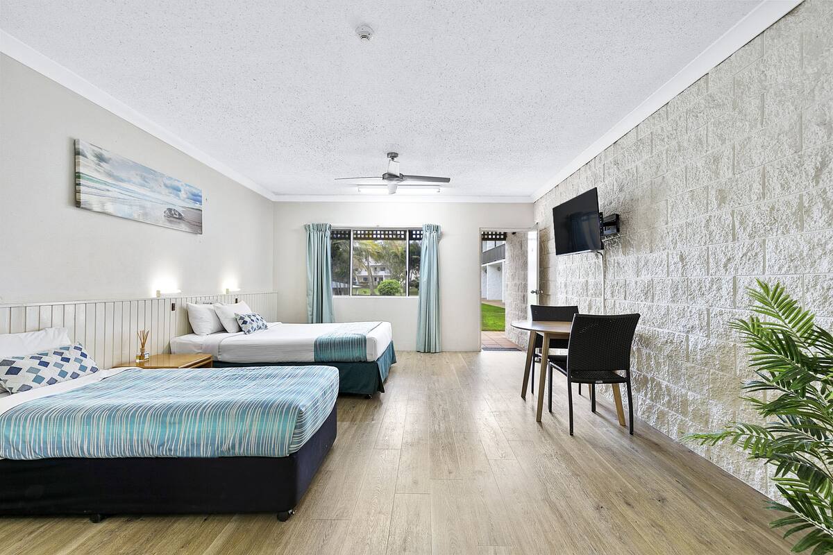 A hotel room with two beds, a desk, a chair, a TV mounted on the wall, and a ceiling fan.