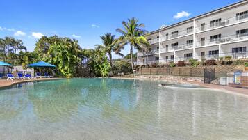 A swimming pool with clear water, surrounded by palm trees and blue umbrellas.