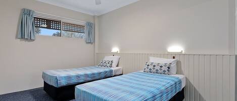 A room with two single beds, a ceiling fan, and a window with curtains.