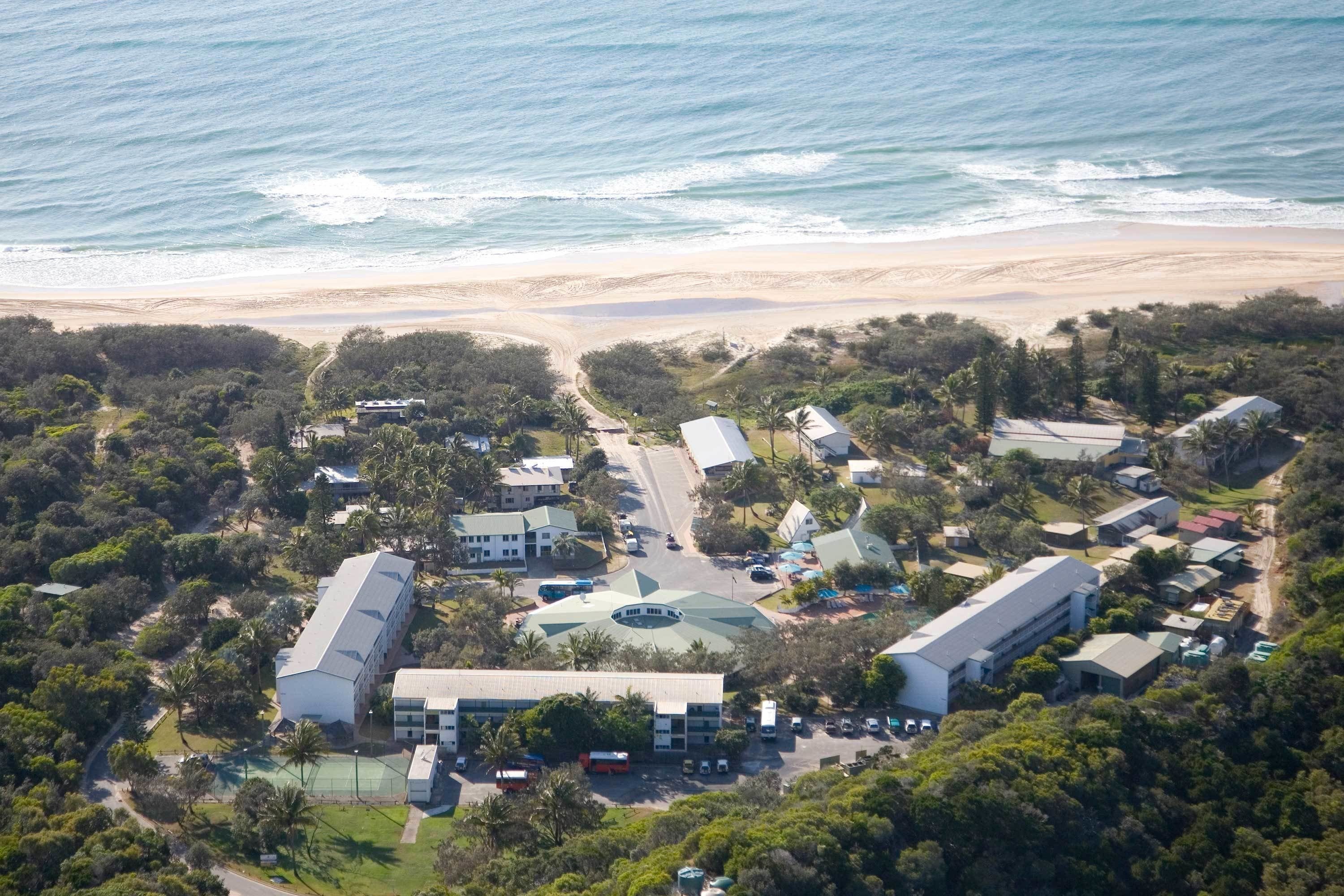 An aerial view of a resort with multiple buildings, a beach, and a tennis court.