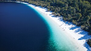 An aerial view of a beach with clear turquoise waters, white sand, and dense forested areas. - K'gari Beach Resort (Eurong)