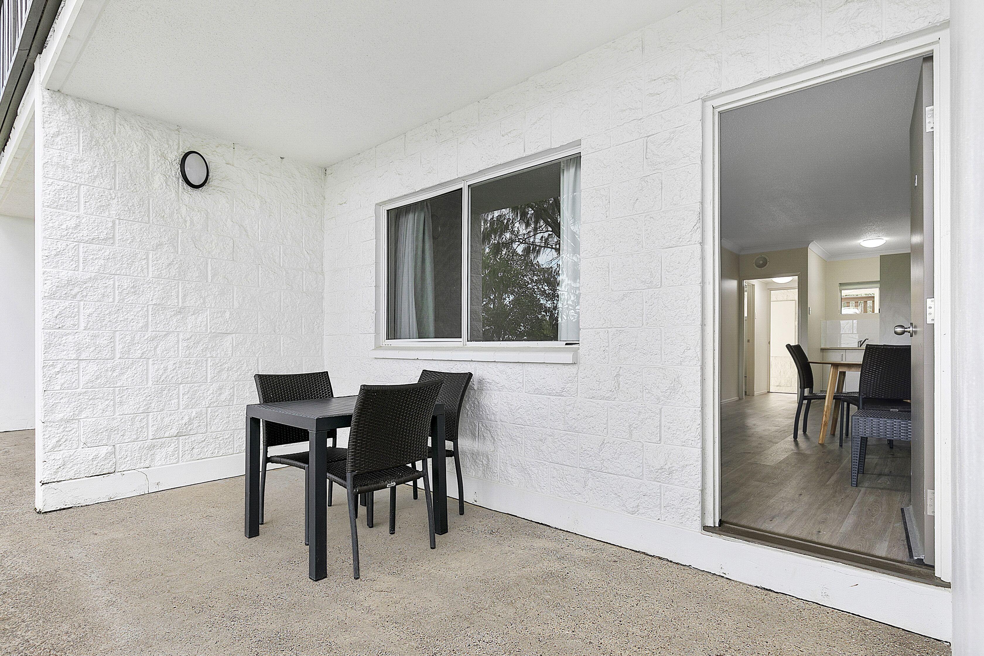 A room with a dining table and chairs, a window with curtains, and a view of another room through a glass door.
