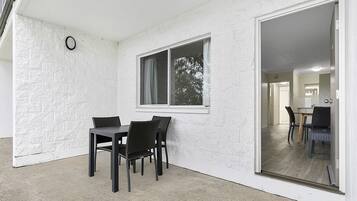 A room with a dining table and chairs, a window with curtains, and a view of another room through a glass door.