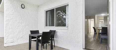 A room with a dining table and chairs, a window with curtains, and a view of another room through a glass door.
