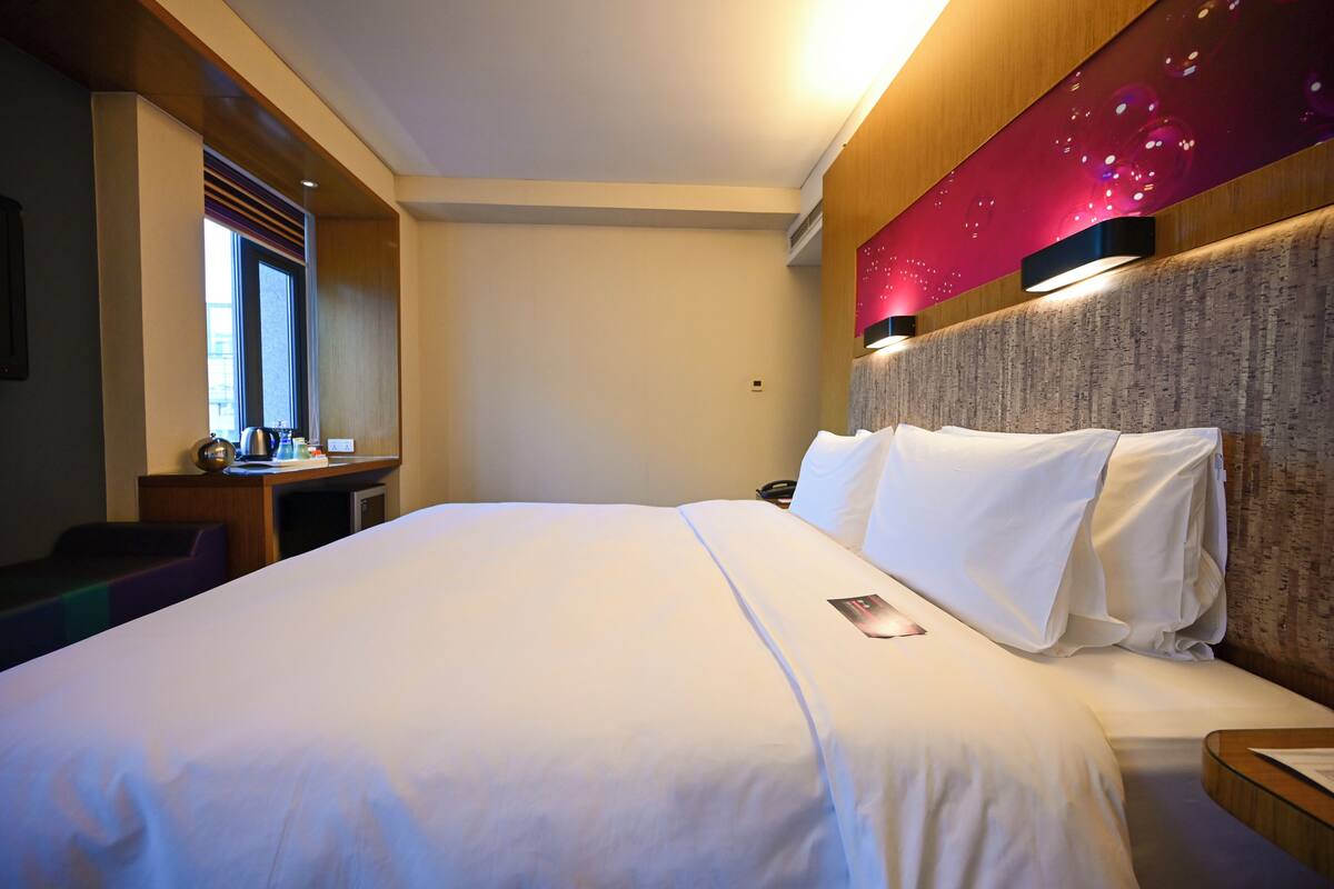 A hotel room with a large bed, a desk with a computer, and a window.