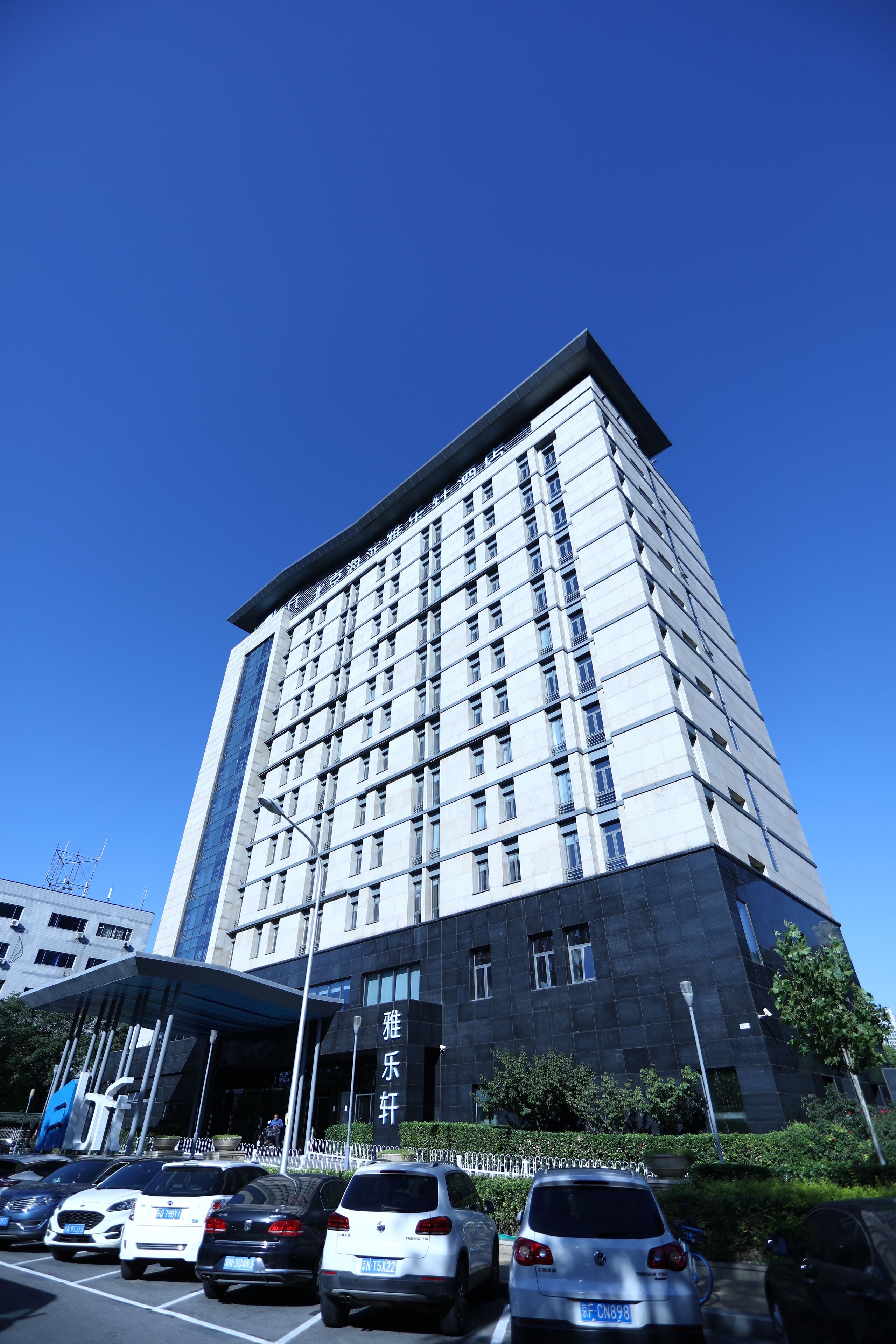 Un edificio moderno con una entrada destacada, varios pisos y un estacionamiento con varios autos.