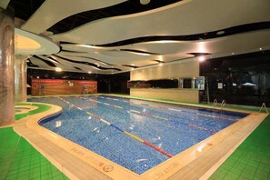 An indoor swimming pool with a tiled floor, a diving board, and a wooden deck area. - Aloft Beijing, Haidian (Beijing)