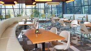 Un comedor moderno con disposición de asientos curva, mesas de vidrio y vistas de la ciudad a través de amplios ventanales.