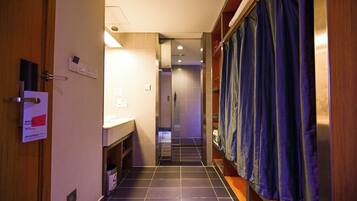 A hotel corridor with a bathroom on the right, a wooden door on the left, and a tiled floor.
