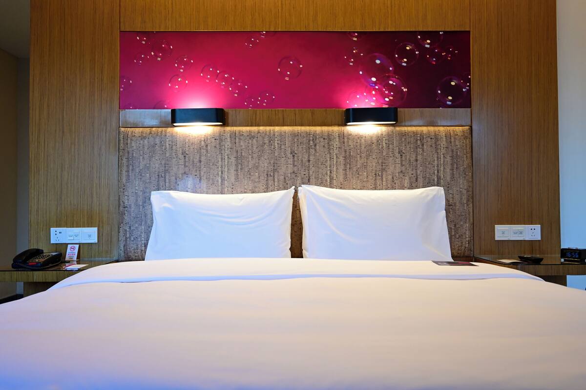 A hotel room with a large bed, two bedside tables, a wall-mounted TV, and a wall with bubble lights.