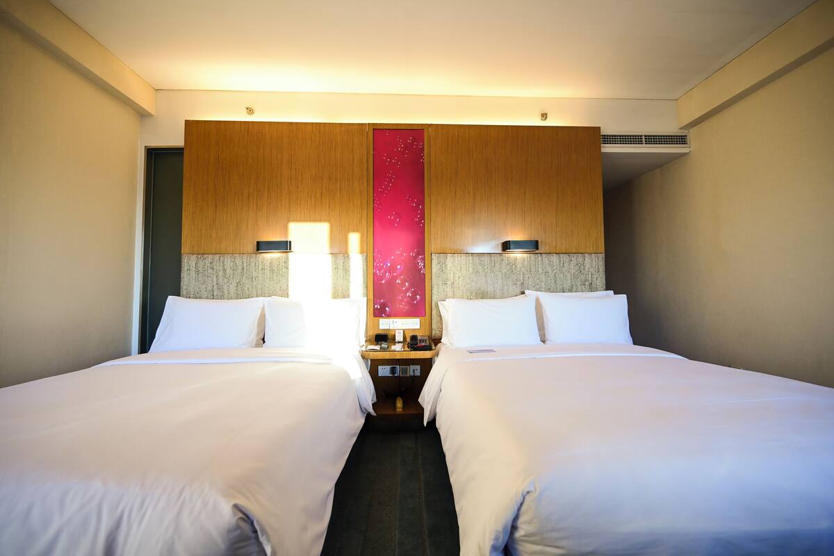 A hotel room with two beds, a wooden accent wall, a red decorative panel, and bedside lamps.