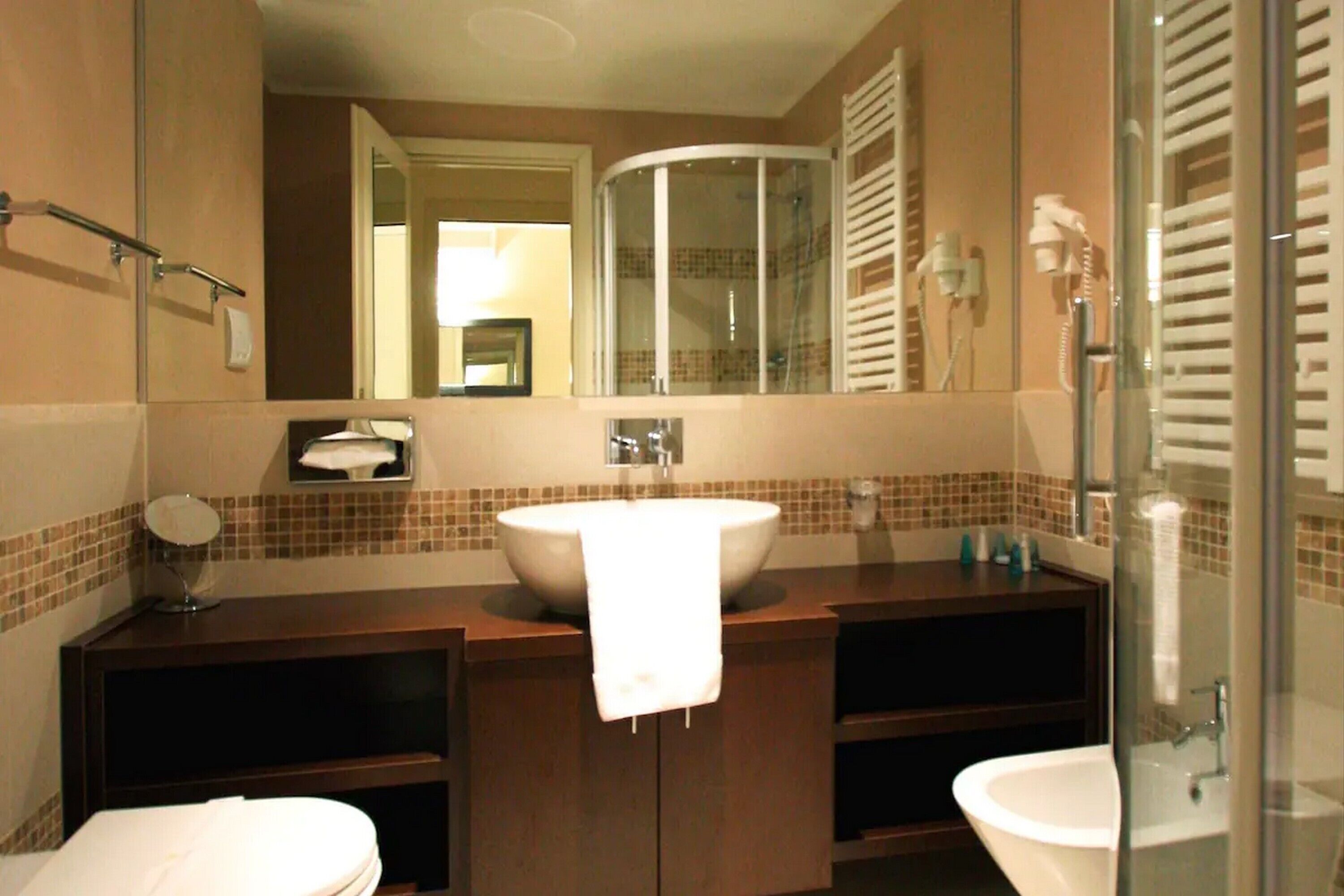 Une salle de bain avec un grand miroir, un lavabo, des toilettes et un espace douche.