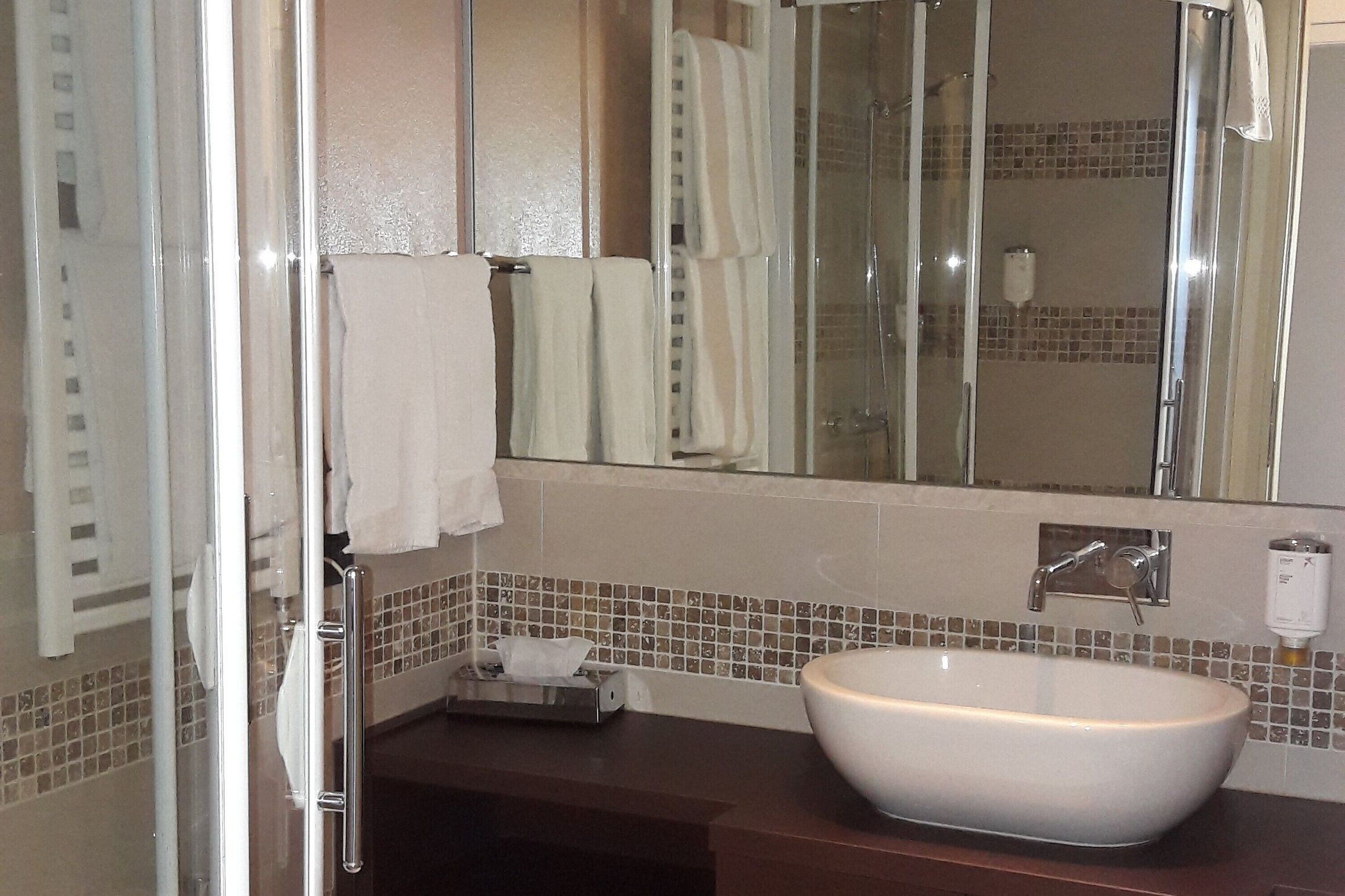 Un baño con un espejo grande, un lavamanos blanco y una cabina de ducha de vidrio.