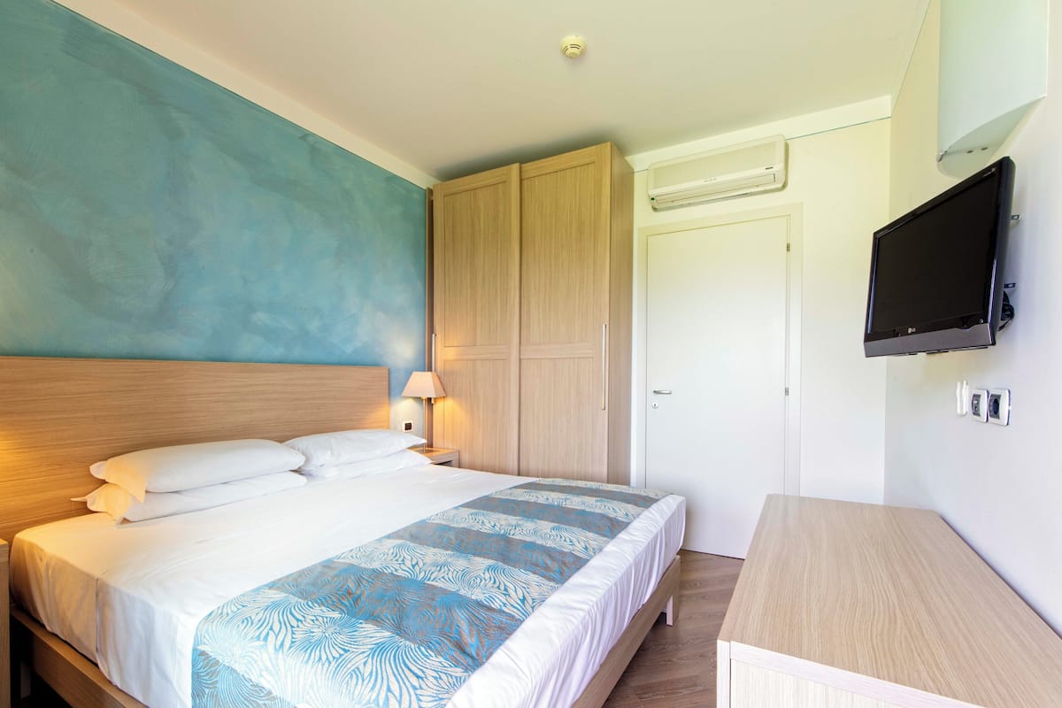 Un dormitorio con cama, mesita de noche, televisor montado en la pared y armario.