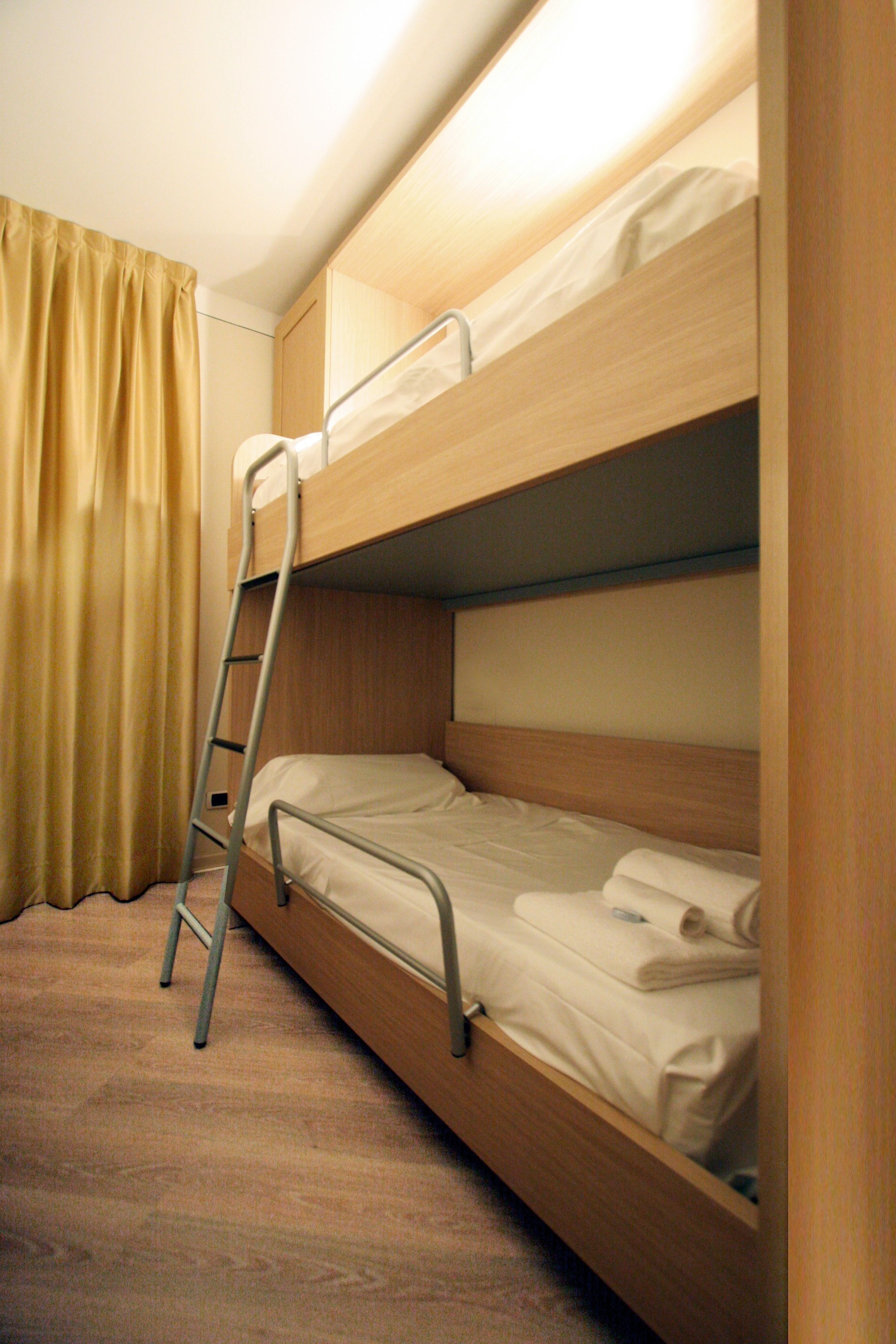 Ein Stockbett mit einer Leiter, einem Holz-Kopfteil und einem beige farbenen Vorhang.