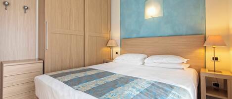 A hotel room with a large bed, wooden wardrobe, bedside tables with lamps, and an air conditioning unit on the wall.