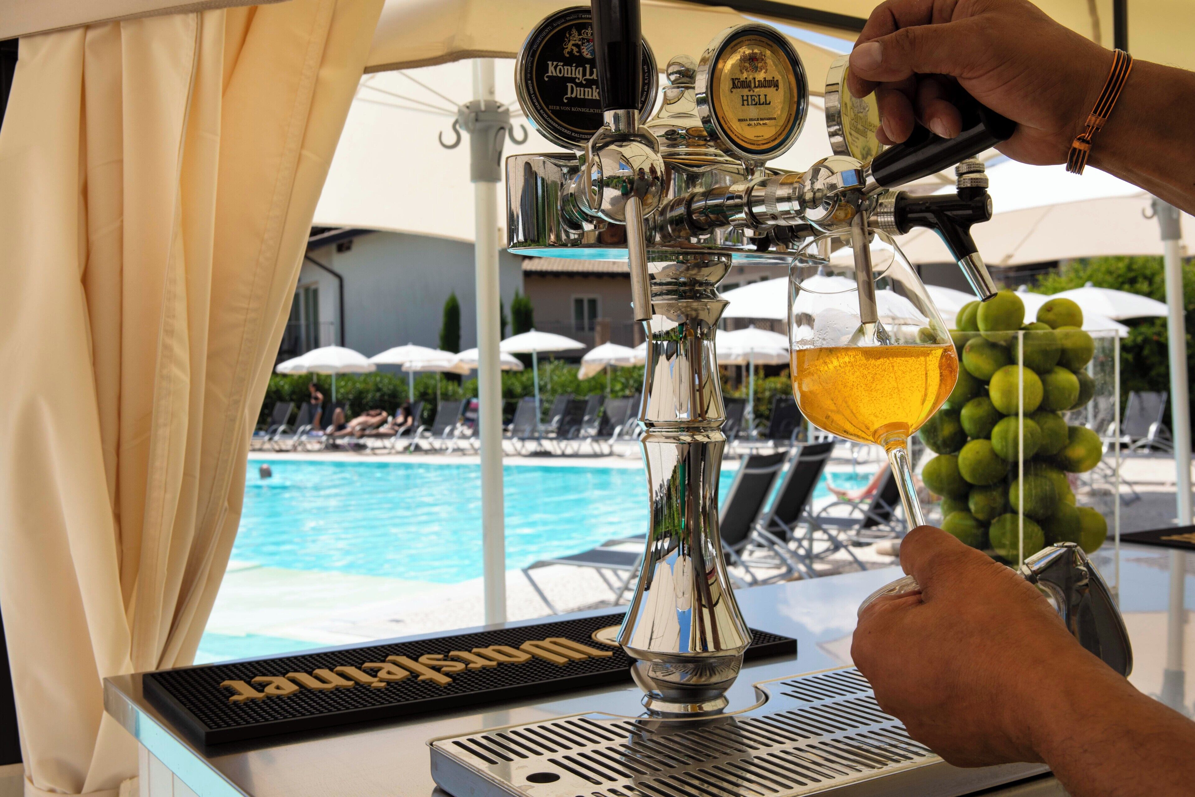Un grifo de cerveza con dos rótulos, una piscina y sillones de descanso al fondo.