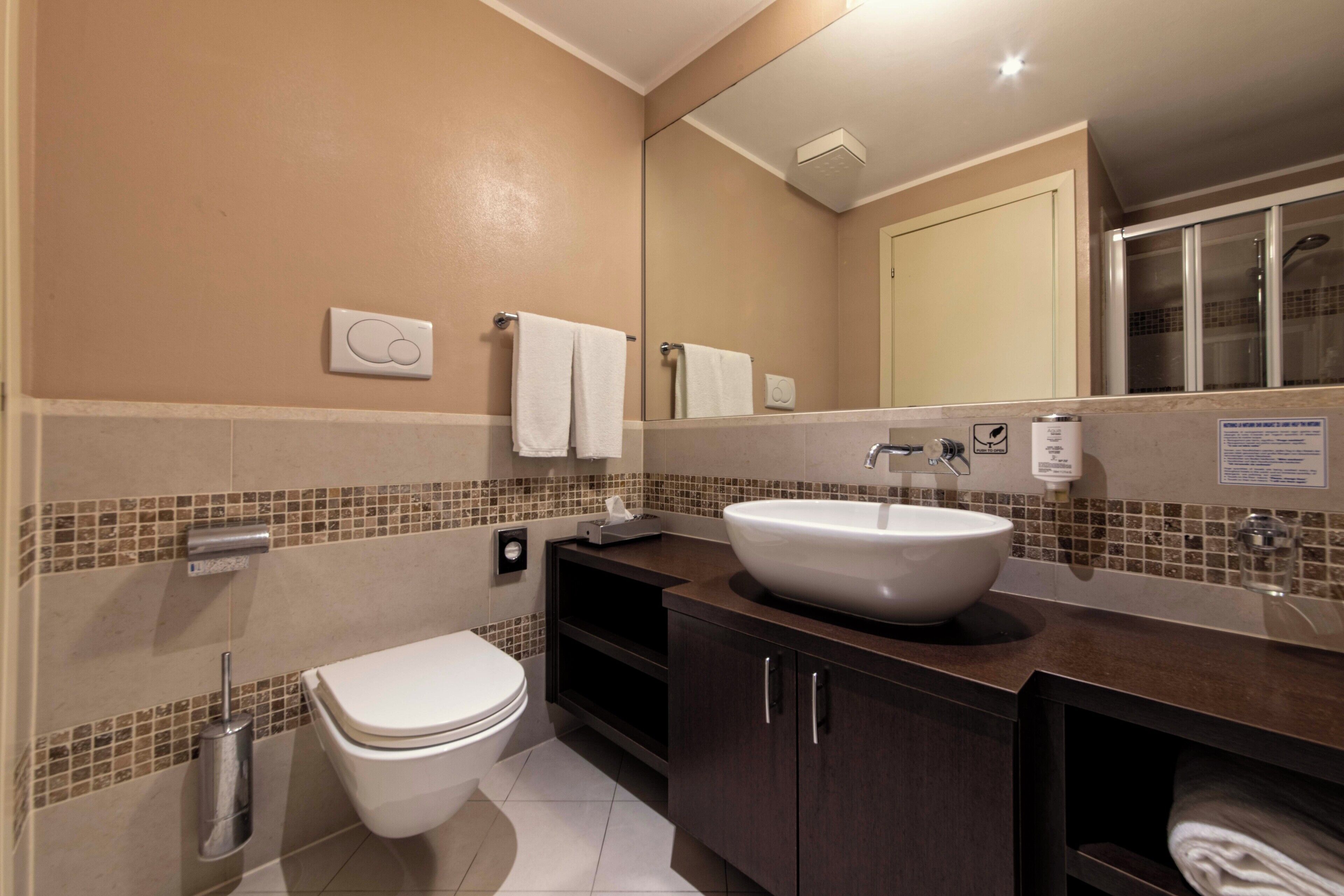 A modern bathroom with a white toilet, a large mirror, a sink, and a shower area.