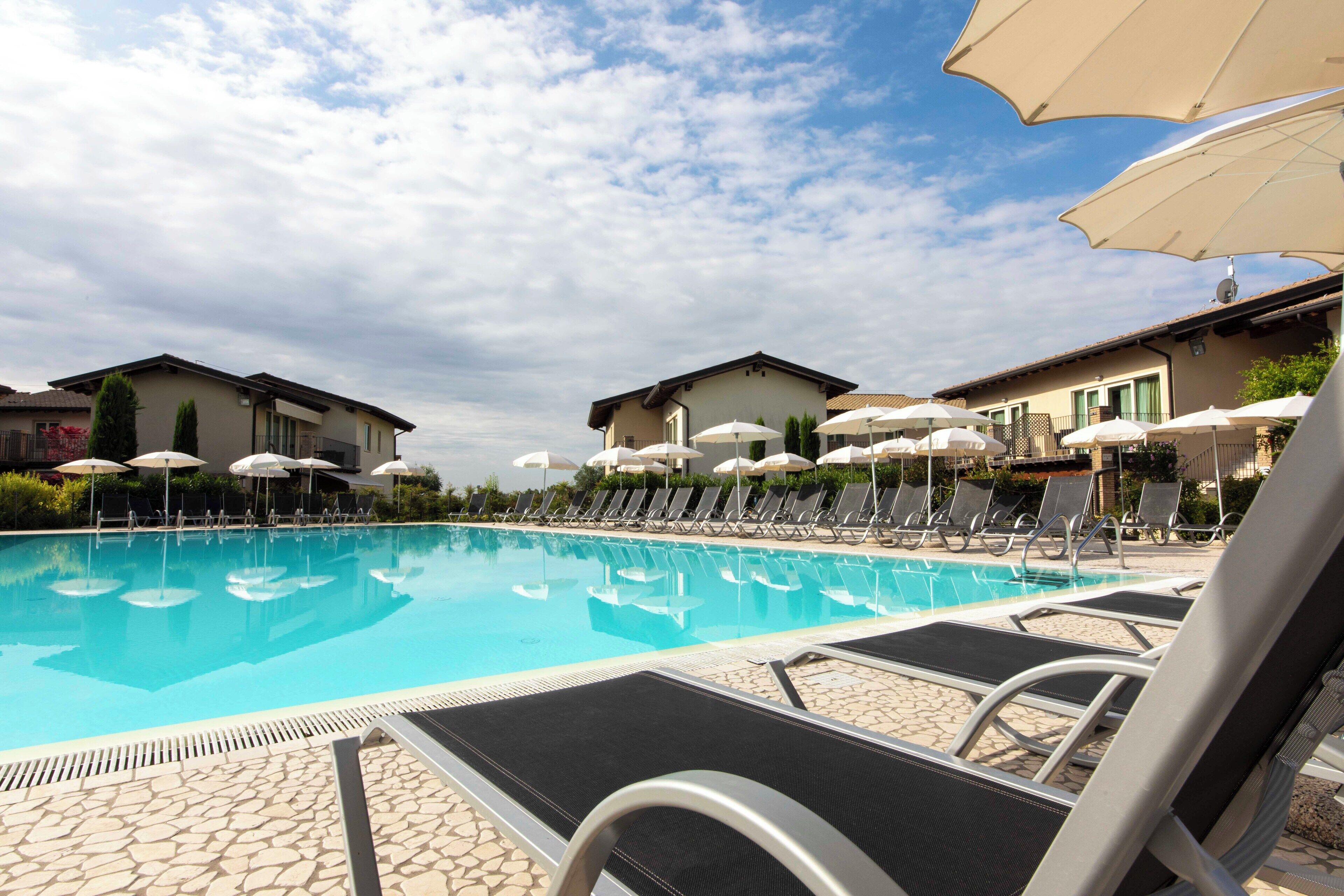 A swimming pool with lounge chairs and umbrellas, surrounded by buildings.