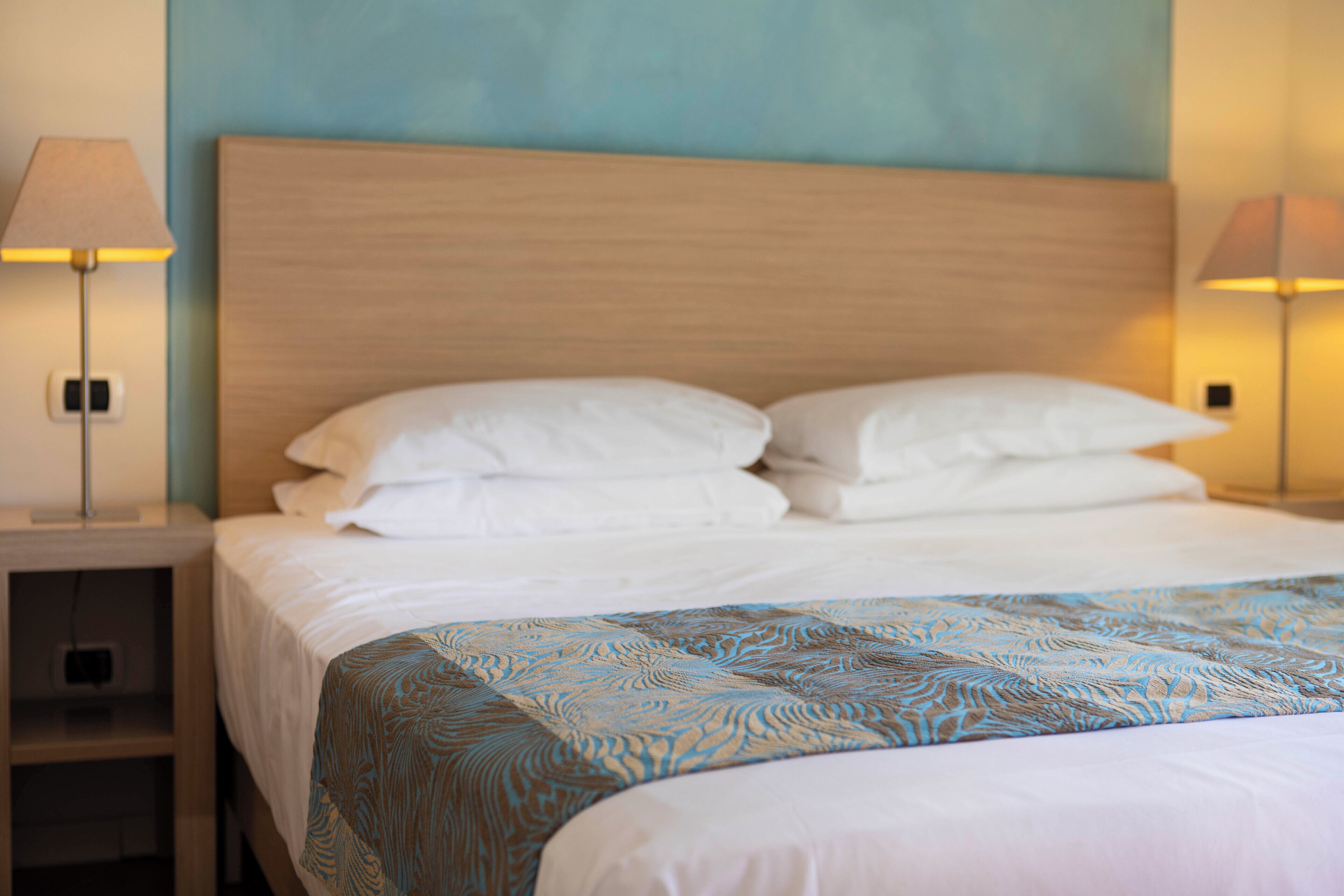A neatly made bed with a patterned bedspread, two bedside lamps, and a wooden headboard.