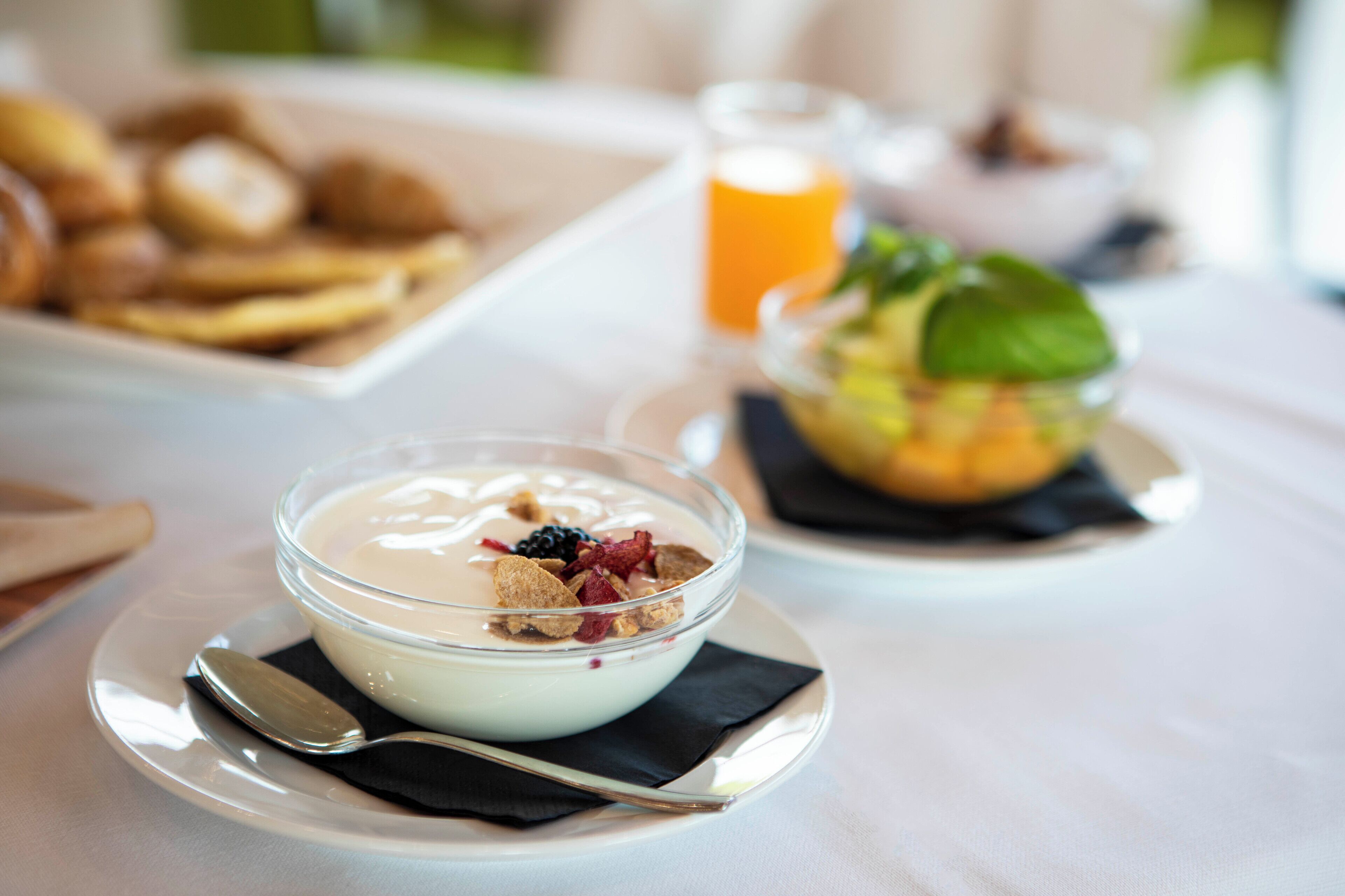 A dessert bowl with yogurt and berries on a white plate, accompanied by a spoon and a napkin.