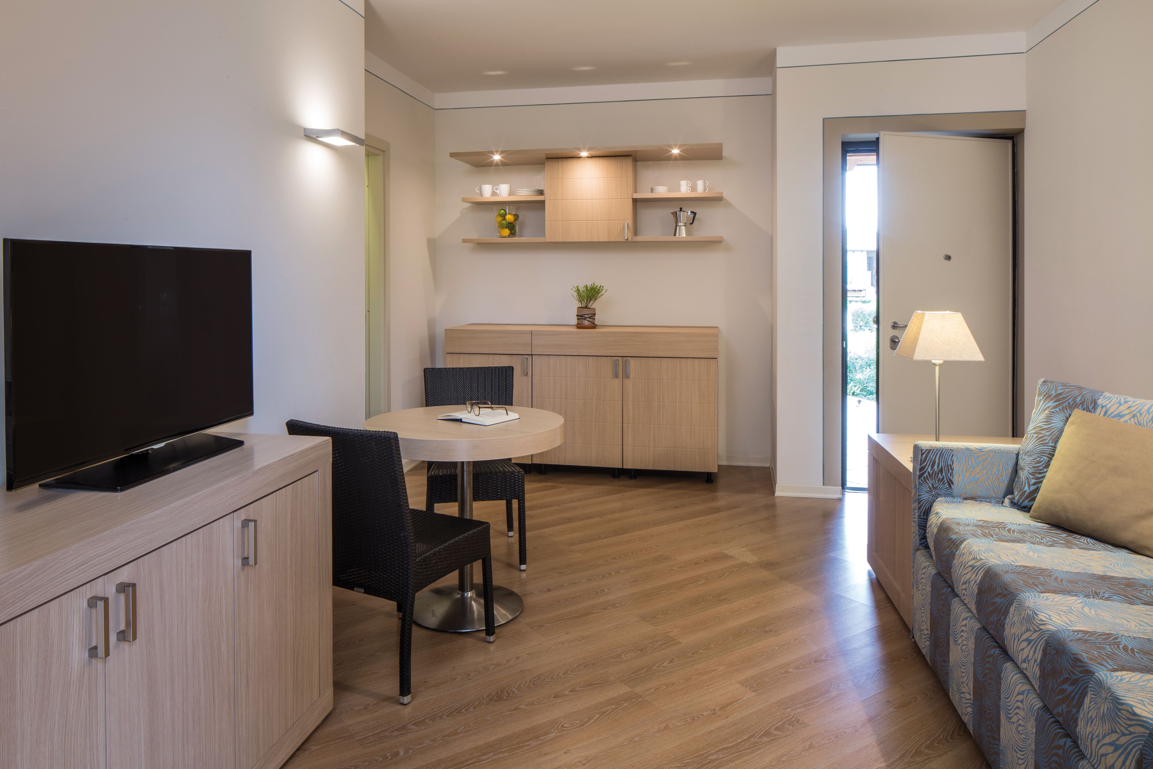 A compact living space with a TV, dining table, chairs, a sofa, and a kitchenette.