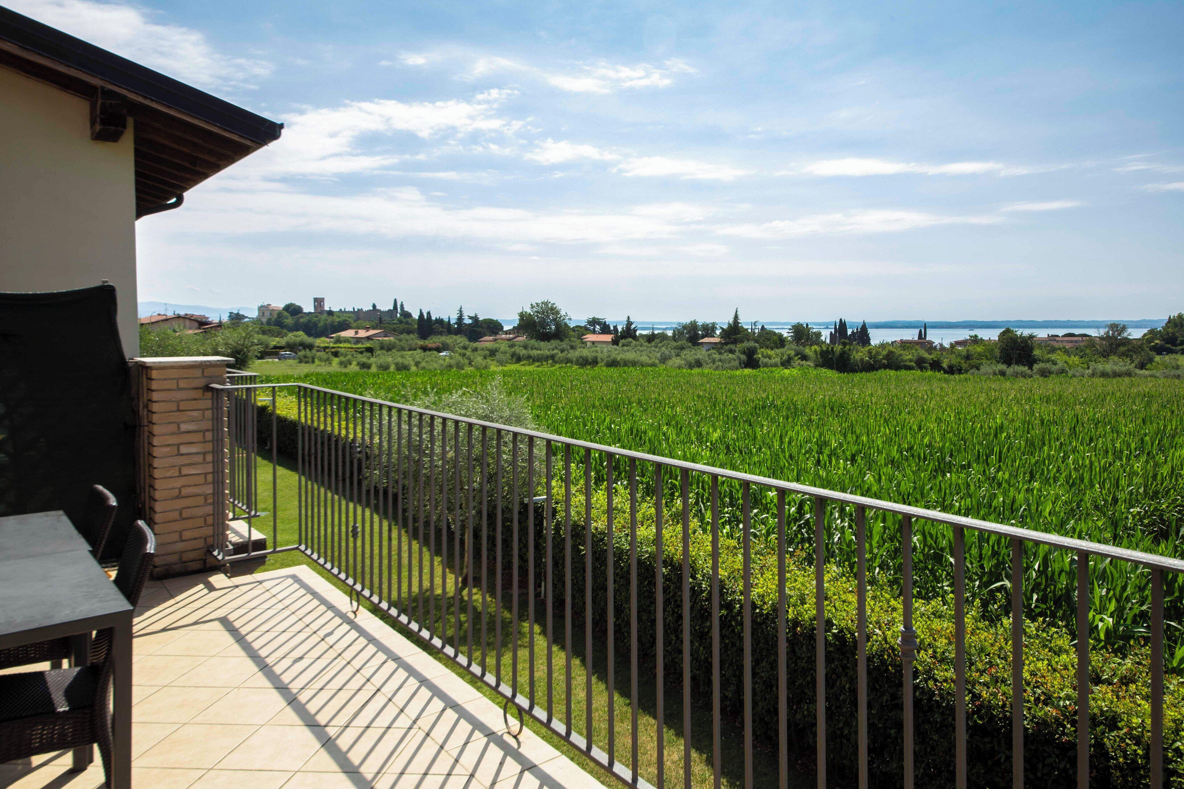 A balcony with a view of a green field and distant buildings.