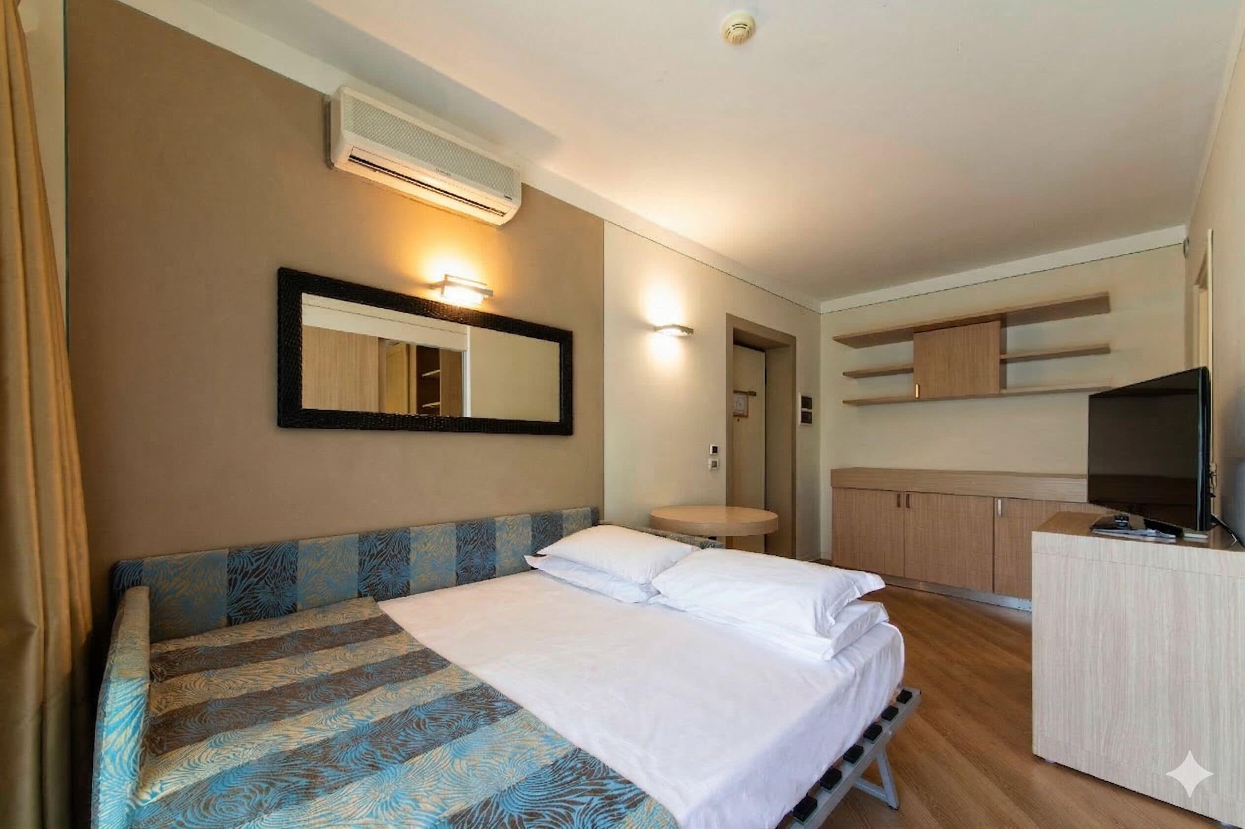 A hotel room with a bed, a TV, a desk, and a mirror.