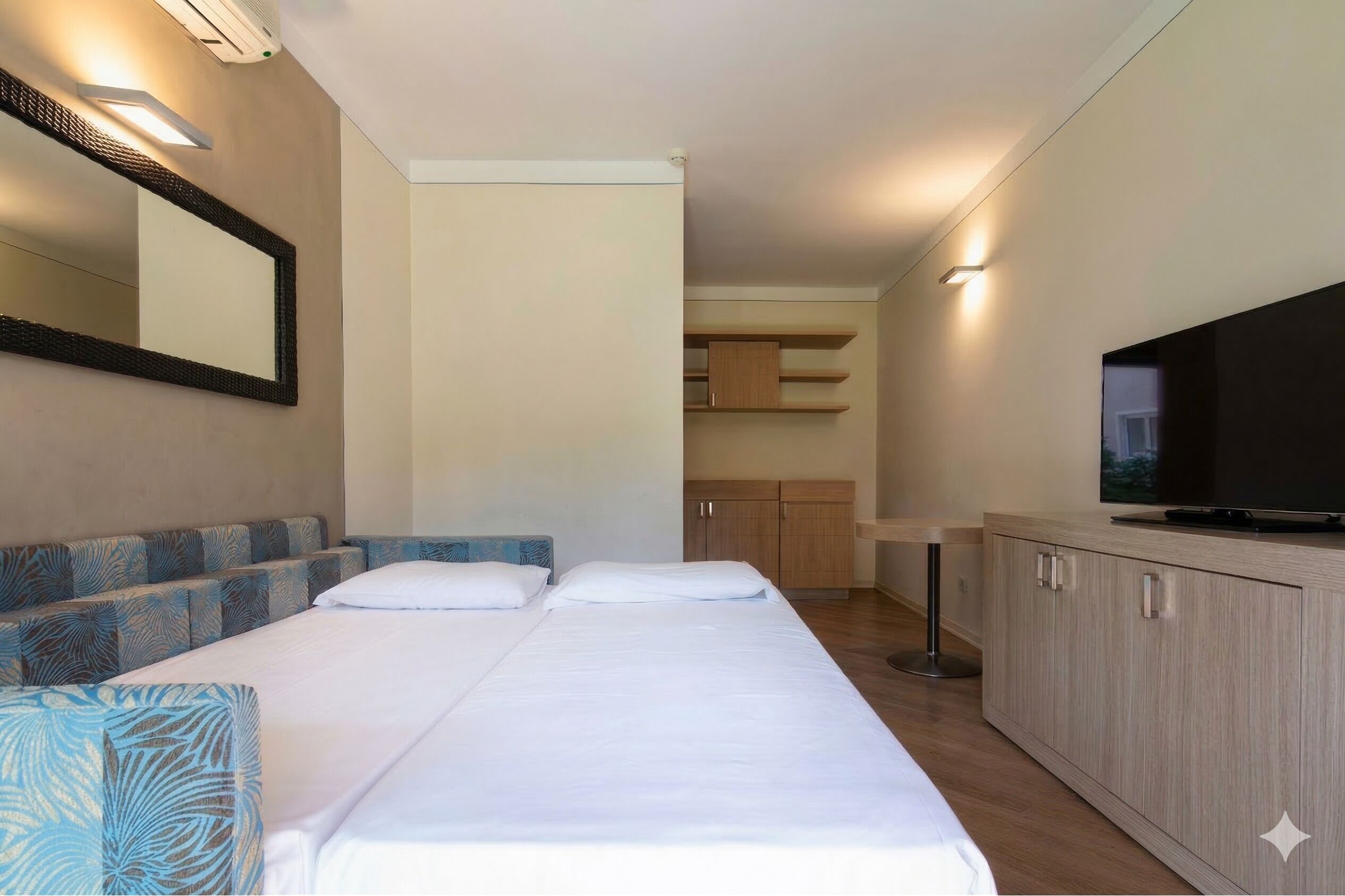Ein Hotelzimmer mit zwei Betten, einem Fernseher, einem Schrank und einem Spiegel.