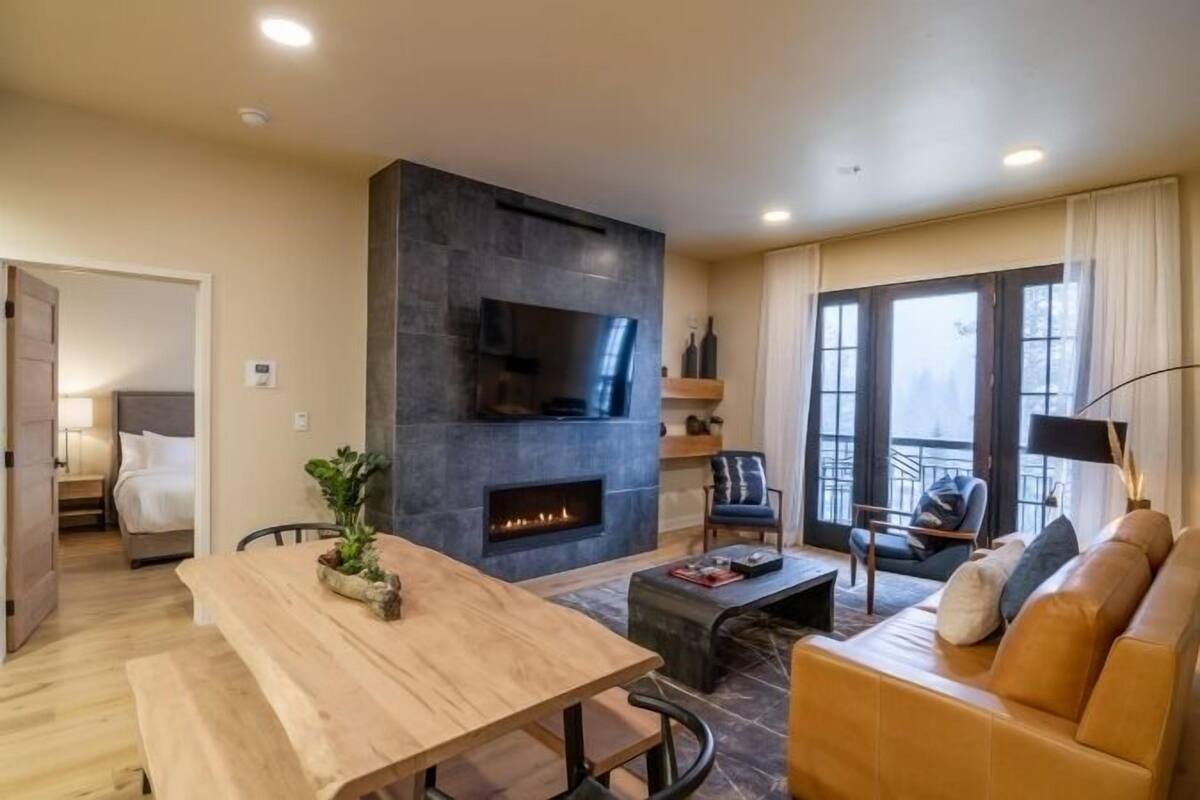 A modern living room with a fireplace, a sofa, a dining table, and a TV mounted on the wall.
