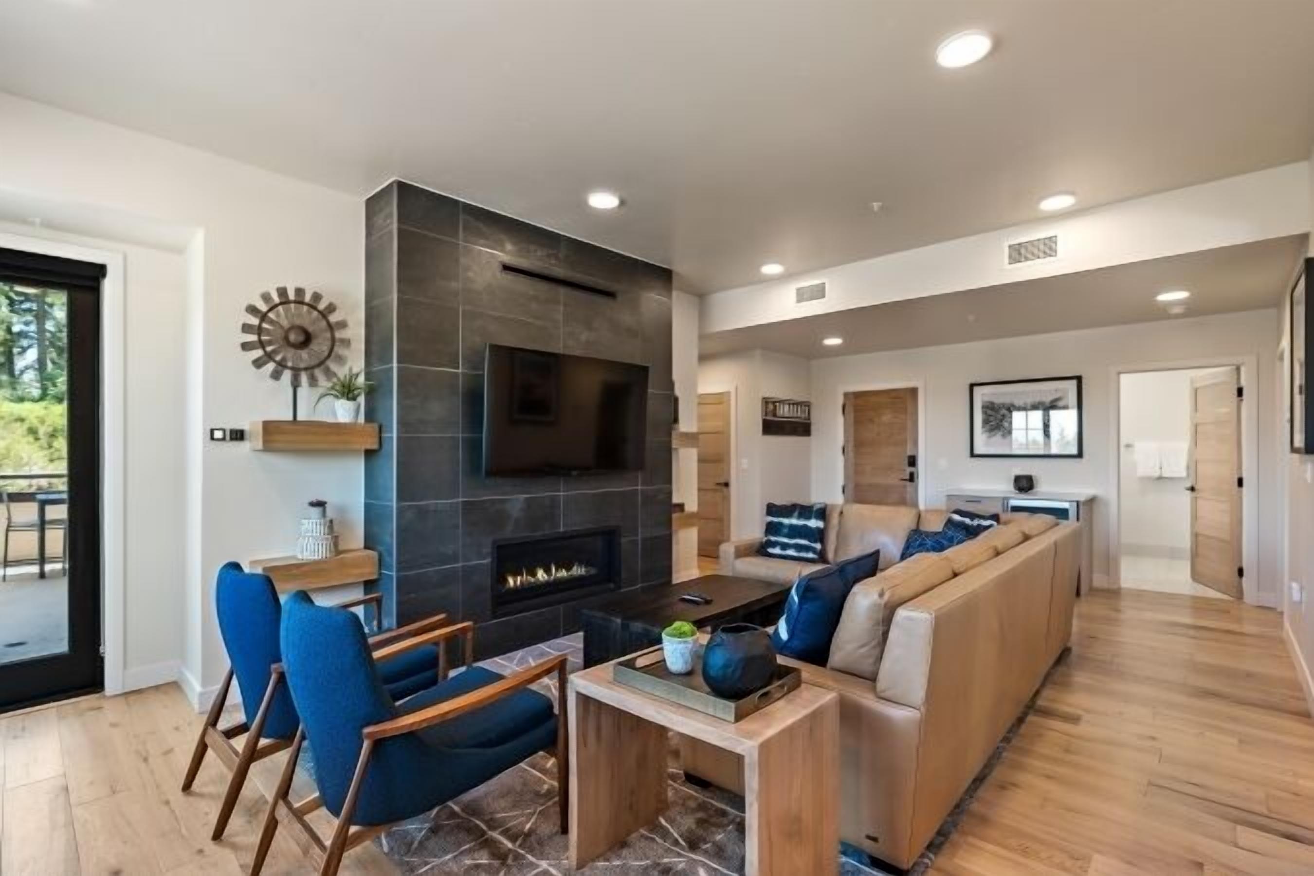 Una sala de estar moderna con chimenea, sillas azules, una mesa de centro de madera y un sofá grande.