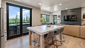 A modern kitchen with a large TV, wooden flooring, and a dining area with a white table and chairs.