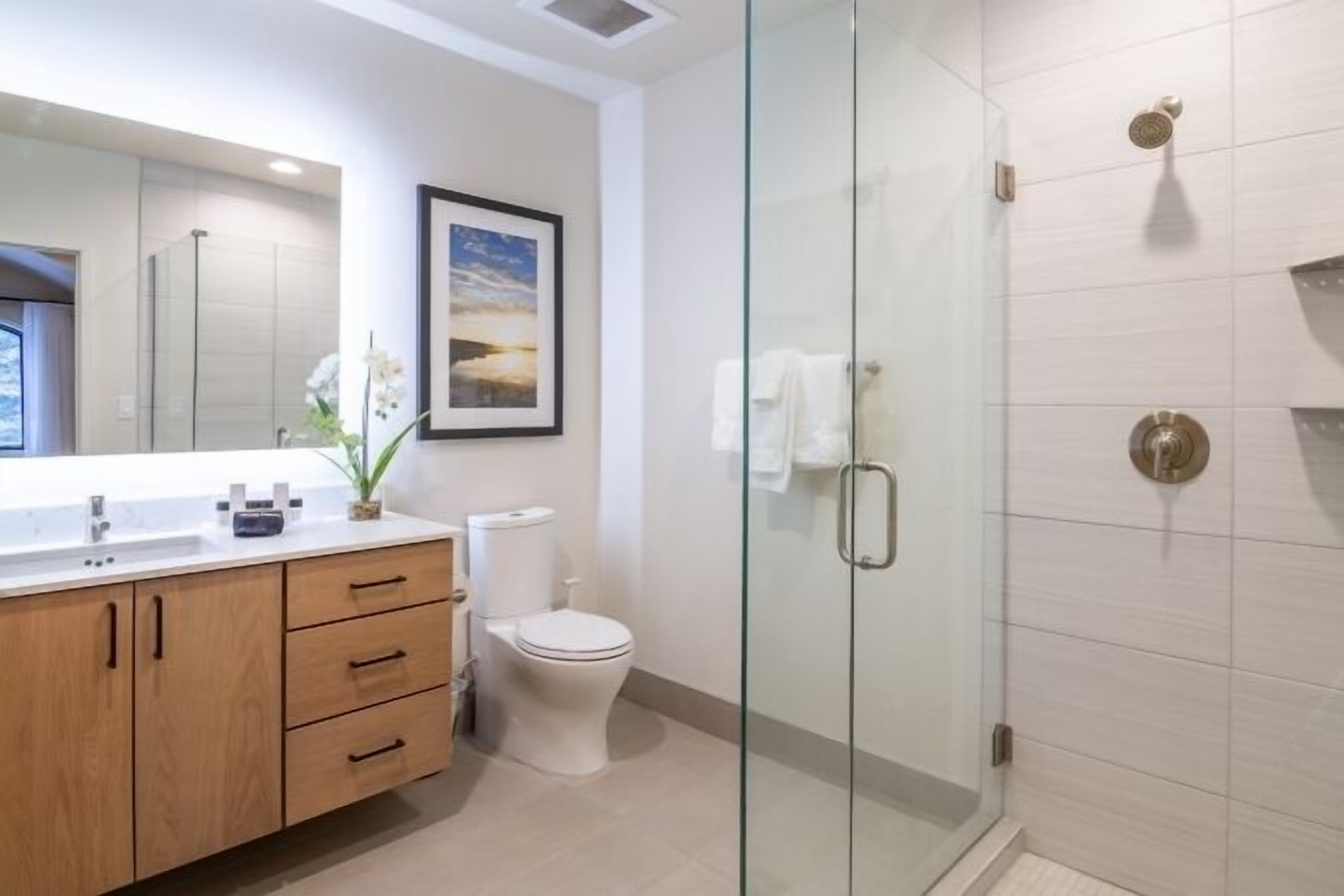 A modern bathroom with a glass-enclosed shower, a white toilet, and a wooden vanity with drawers.