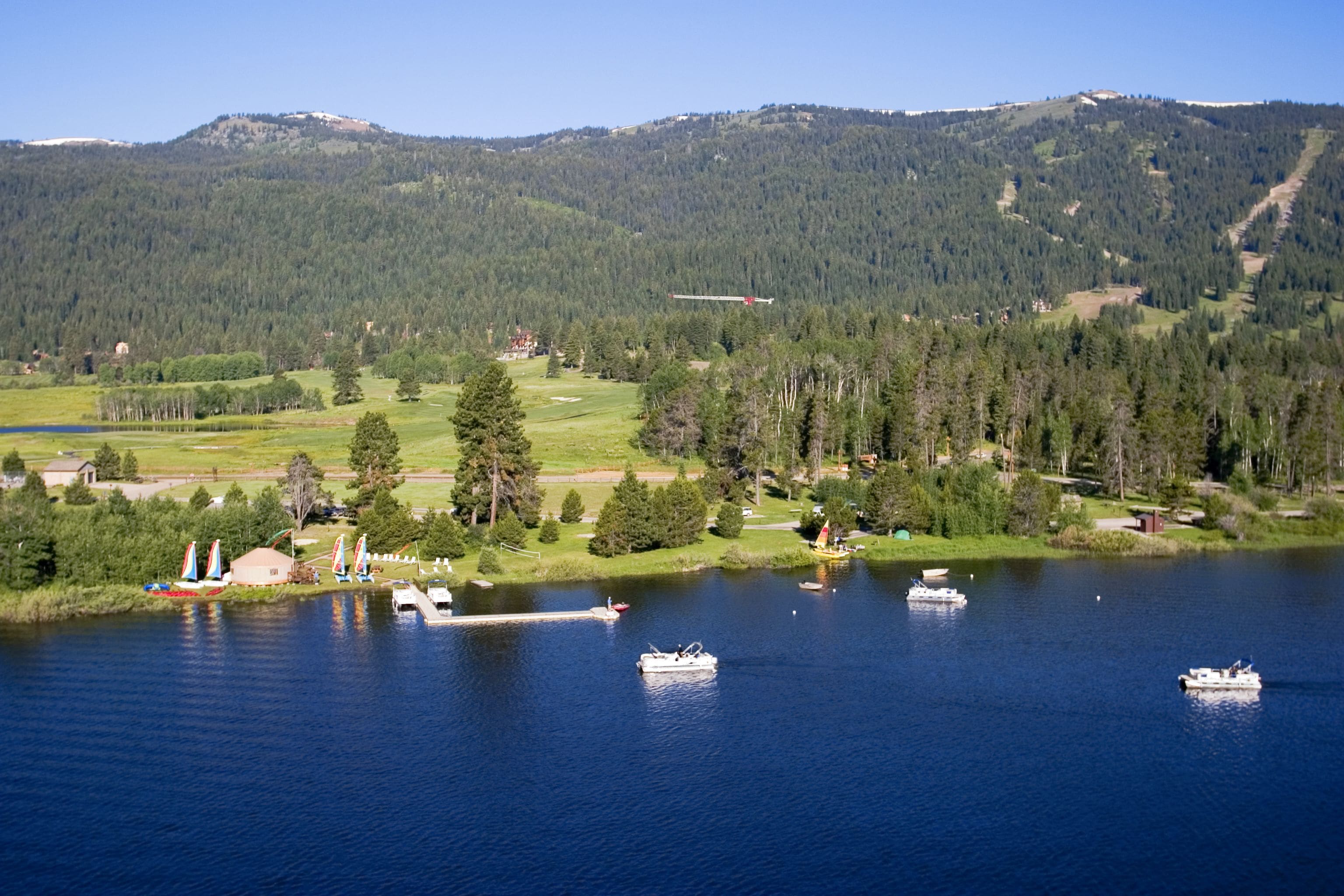 Un lago con barcos, un muelle y una montaña boscosa al fondo.