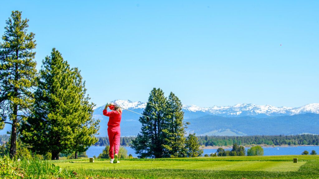 Une personne vêtue de rouge sur un terrain de golf, avec une chaîne de montagnes en arrière-plan.
