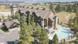 A lodge with a clock tower, a swimming pool, and a view of a lake and mountains.