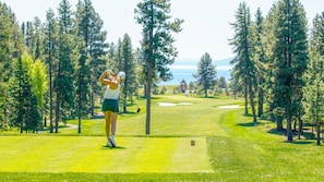 A golf course with a clear path, surrounded by trees and a distant view of a body of water.