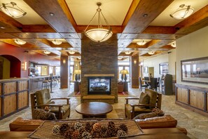 Un hall d’entrée spacieux avec une cheminée en pierre, des poutres en bois au plafond et un coin bar.