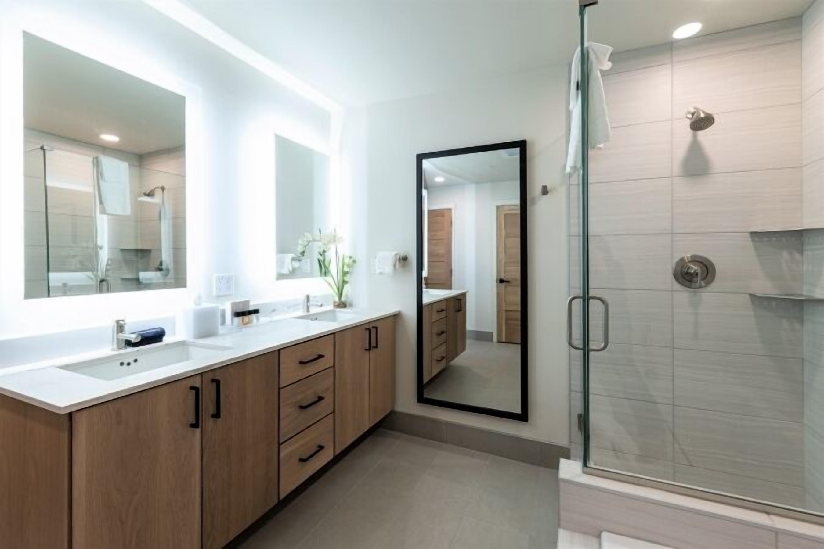 A modern bathroom with two sinks, a large mirror, and a glass-enclosed shower.