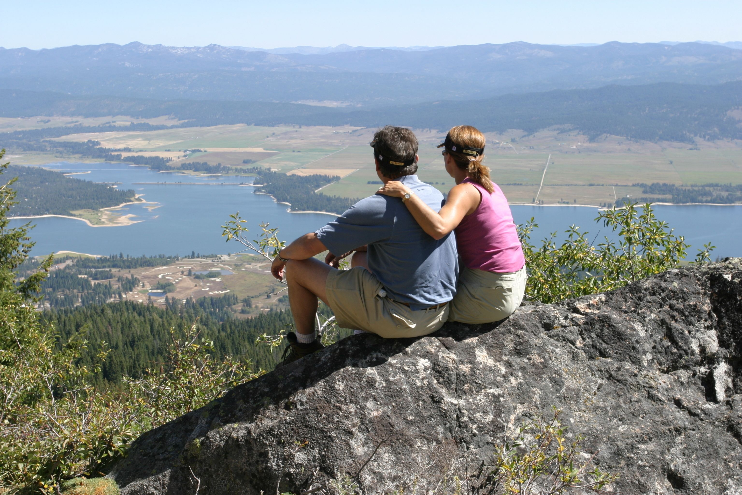 A couple sitting on a rock overlooking a lake and mountains.