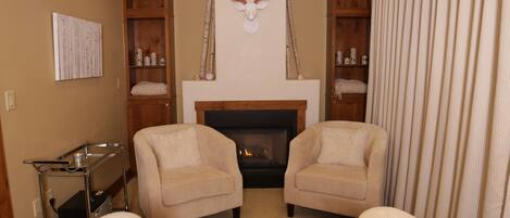 Una habitación acogedora con dos sillones, una chimenea y un armario de madera con estantes.